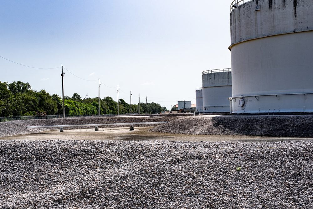 Three white aboveground bulk fuel storage tanks surrounded by an earthen and gravel secondary containment berm, with transfer piping crossing the dike. The containment area is graded to capture any spill from the tanks.