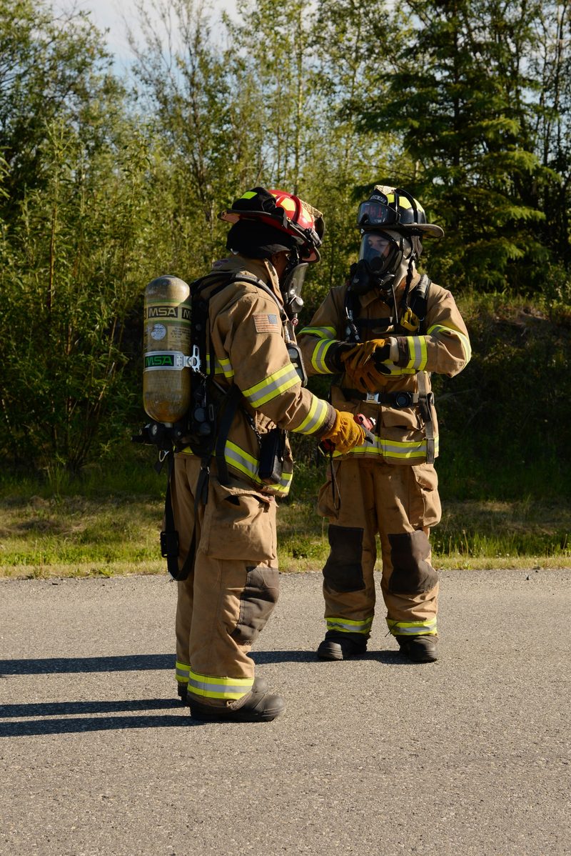 Two firefighters in full bunker gear with self-contained breathing apparatus and full-face masks prepare to approach a simulated fuel spill site.